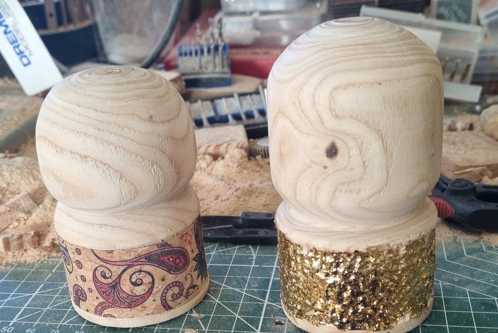 Two inlayed and guilded walking stick toppers with rounded tops, one decorated with paisley pattern, workshop background.